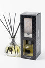 Reed diffuser set with glass bottle and black sticks next to its packaging on a white background