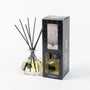 Reed diffuser set with glass bottle and black sticks next to its packaging on a white background