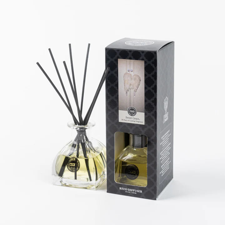 Reed diffuser set with glass bottle and black sticks next to its packaging on a white background