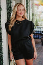 Woman wearing a black outfit standing outdoors near greenery