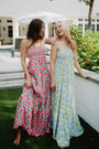Two women in floral dresses standing outdoors near a pool.