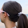 Person with a ponytail wearing pink sunglasses, beach in the background