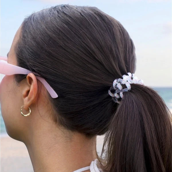 Person with a ponytail wearing pink sunglasses, beach in the background