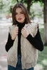 Woman wearing a beige quilted vest over a black top with a blurred outdoor background
