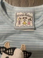 Close-up of a striped baby t-shirt with a cartoon patch on the chest, featuring a white and light blue horizontal stripe pattern and a cute character patch.