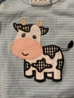 A close-up of a cow applique patch on a gray and white striped fabric background.
