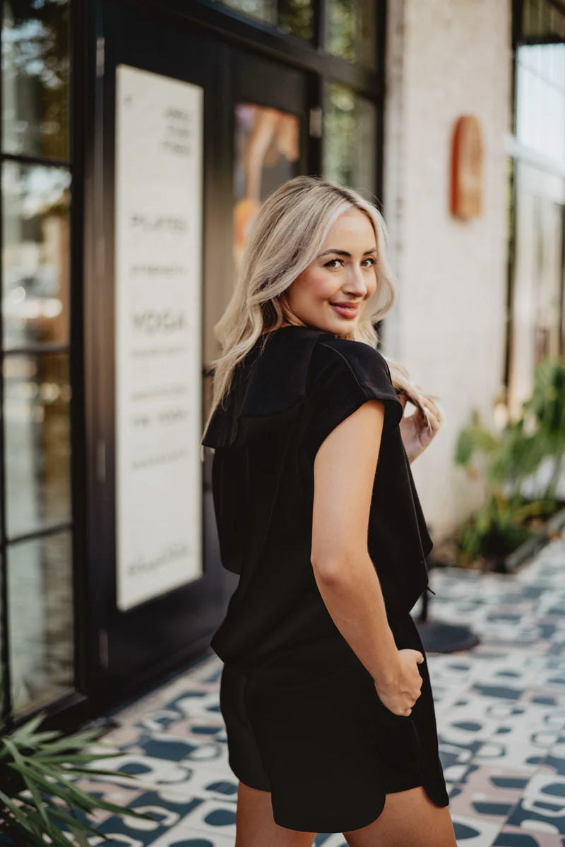 Woman in a black outfit standing in front of a building entrance.