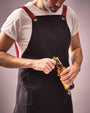 Person in a black apron opening a bottle with a neutral background
