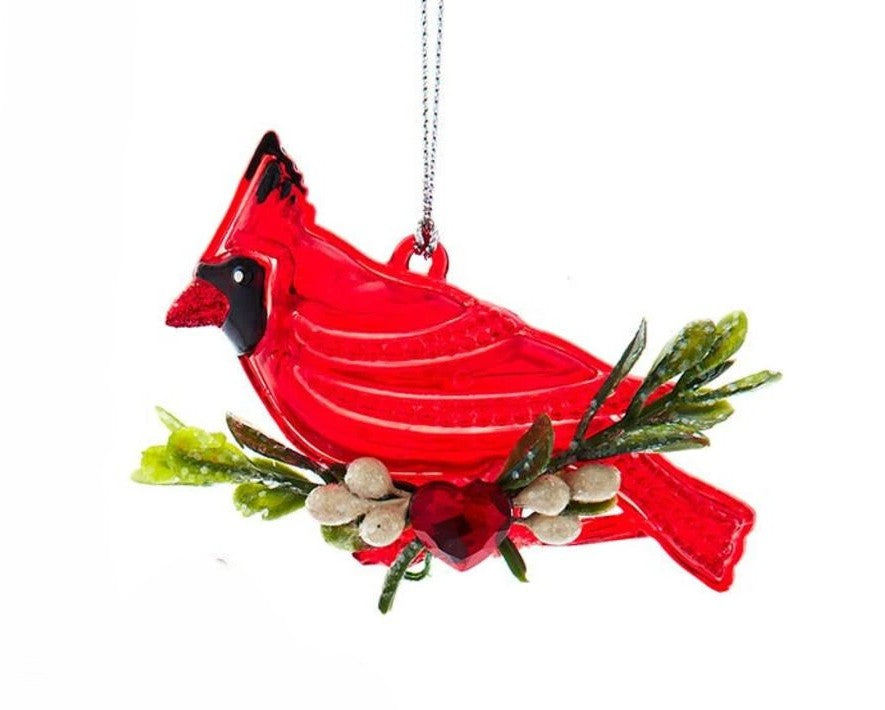 A red cardinal bird Christmas ornament with green pine branches, white berries, and a hanging loop on a white background.