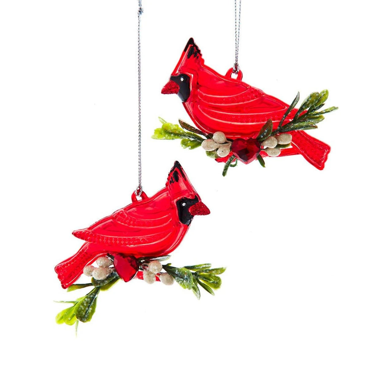 Two red cardinal bird ornaments hanging from silver strings, each perched on a small green branch with white berries, shown on a plain white background.