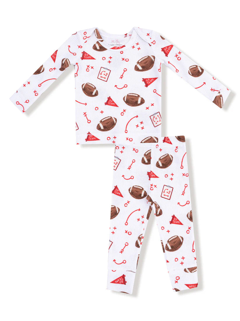 A two-piece baby pajama set featuring a long-sleeve top and matching pants in white, decorated with a red and brown football-themed print including footballs, party hats, and sports icons.