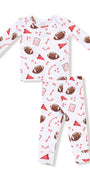 A two-piece baby pajama set featuring a long-sleeve top and matching pants in white, decorated with a red and brown football-themed print including footballs, party hats, and sports icons.