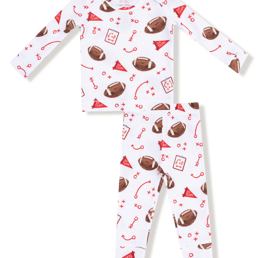A two-piece baby pajama set featuring a long-sleeve top and matching pants in white, decorated with a red and brown football-themed print including footballs, party hats, and sports icons.