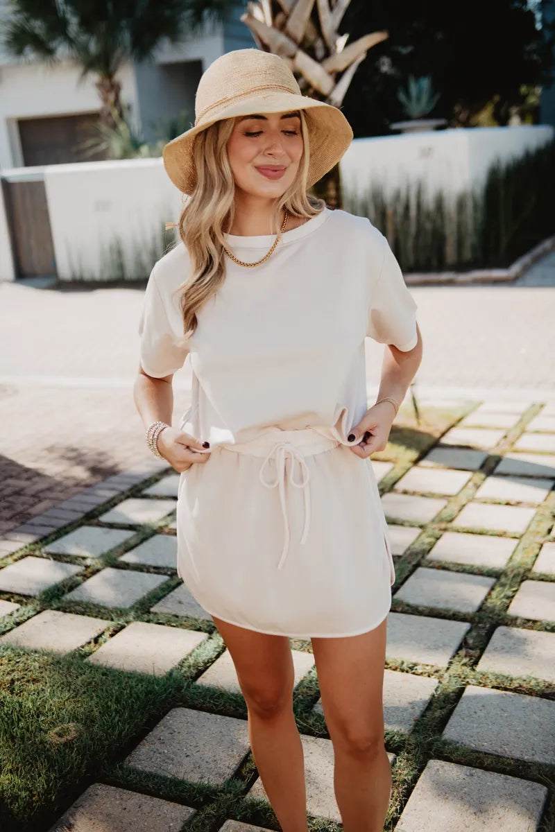 Woman wearing a white outfit and beige hat outdoors on a sunny day.